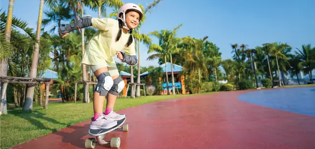 Child skateboarding on a red track lined with palms